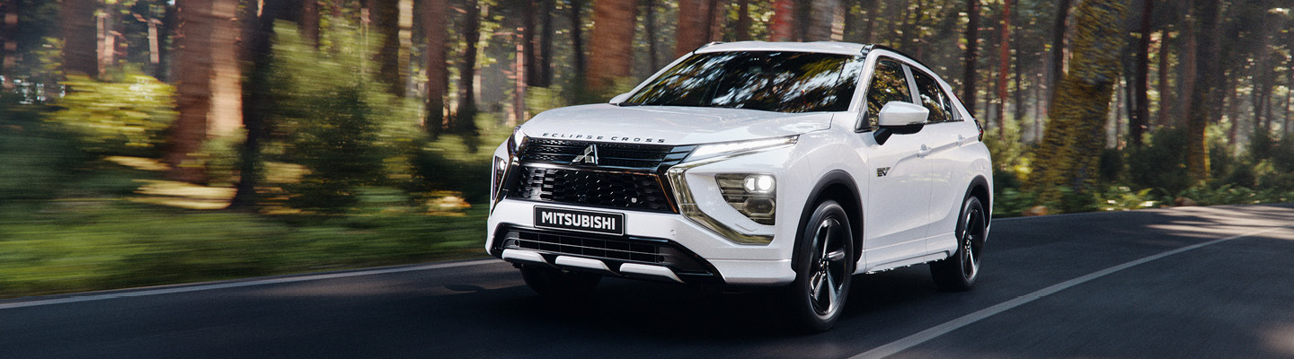 Mars_Hjulskifte_1440x400 Vit Mitsubishi Cross Plug-in Hybrid kör på en väg bredvid solig skog