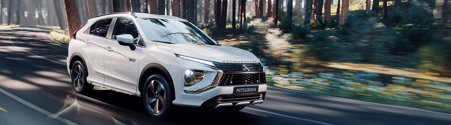 Maj_vindruta_se_1440x400 Vit Mitsubishi Eclipse Cross kör på väg genom solig skog