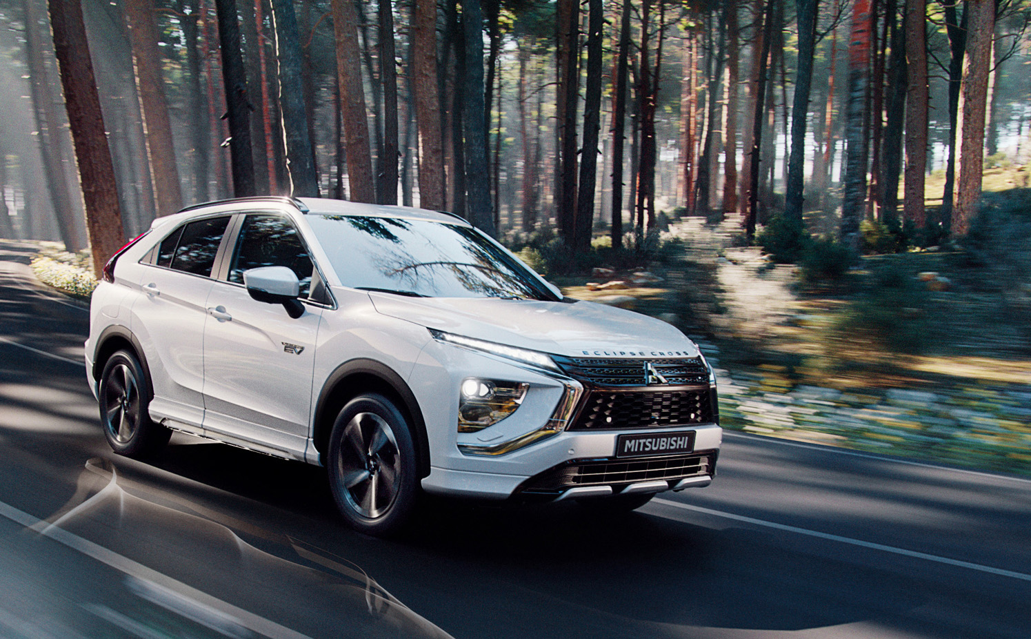 Vit Mitsubishi Eclipse Cross kör på väg genom solig skog