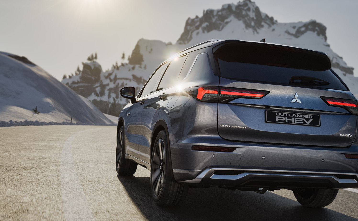 Mitsubishi Outlander kör på en asfalterad väg med berg och snö i bakgrunden