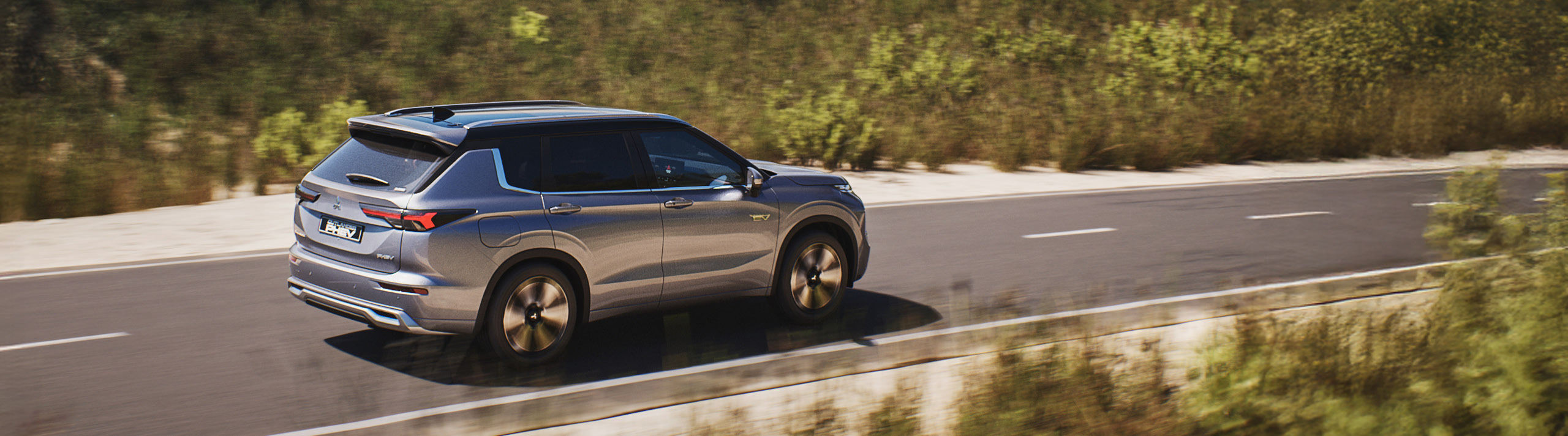 Mitsubishi Outlander kör på en asfalterad väg med berg och snö i bakgrunden